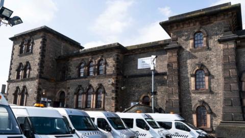 A general view of Wandsworth prison. It is an imposing brick building. A row of prison vans are by the entrance
