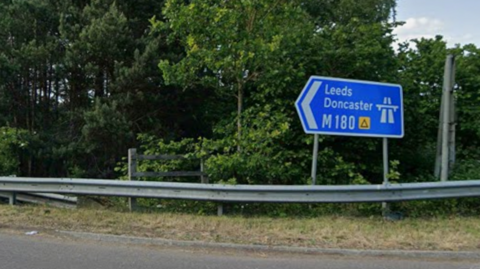 A blue motorway road sign at the slip road to the westbound M180 at the Woodhouse interchange. The sign reads Leeds Doncaster M180