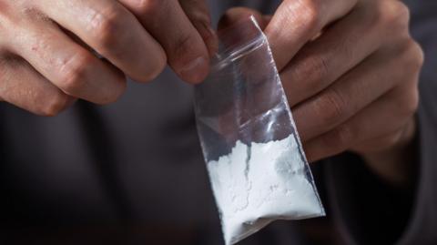 A person opens a small plastic packet of a white powder representing cocaine.