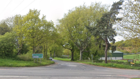 The A614 at the junction with Snape Lane. Trees line the road.