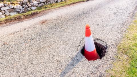 A traffic cone sitting in a large pothole on the Isle of Skye