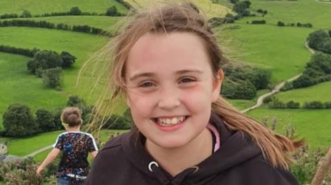 Young girl with long brown hair and black hoodie out in the countryside