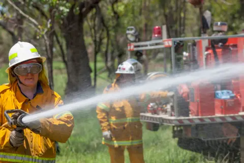 Two Australian firefighters - one holds and sprays a hose