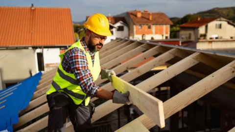 Builder placing a plank on a new roof