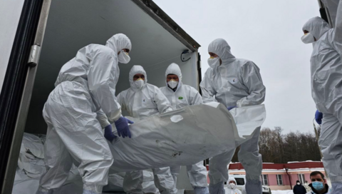 Officials in white overalls that cover their heads and wearing face mask carry a white stretcher presumably containing a body being unloaded from what looks like a truck