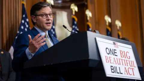 House Speaker Mike Johnson gestures as he speaks during a press conference after passing the bill, a sign on the lecturn reads 'one big beautiful bill act' 