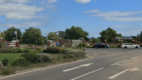 Google view of the road outside the Southview Leisure Park. There is a wall at the entrance with flags, and arrows on the main road indicating a right turn on the other side.