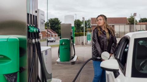 A young woman fills up her car at a petrol station