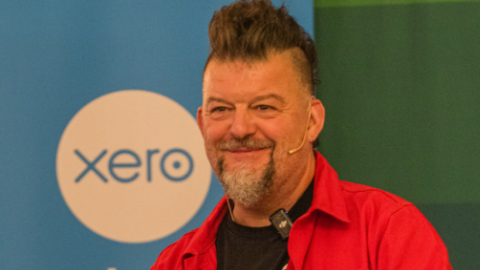 Stefan Thomas at a public speaking event, wearing two microphones. He has a red shirt on.