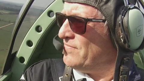 Trevor Bailey flying a plane. He has green headphones and sunglasses on.