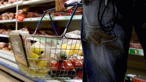 A person holding a shopping basket in a supermarket.