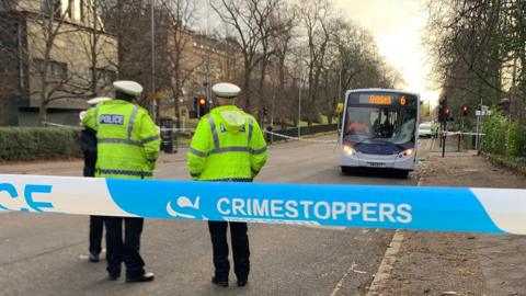 three police officers behind cordon tape with bus in background