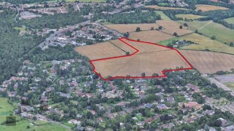 An aerial photo of houses with a parcel of land bordered by a red line.