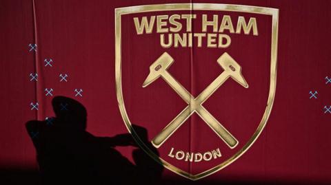 A silhouetted fan taking a picture of the West Ham badge