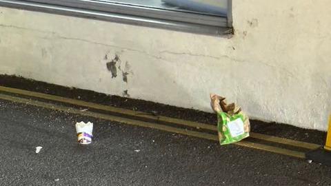 A McFlurry cup and a McDonalds brown bag lie on the edge of a road with double yellow lines along it in front of a white painted building.