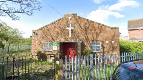 Stowlawn Methodist Church a brick building with a white cross on the front behind a silver fence