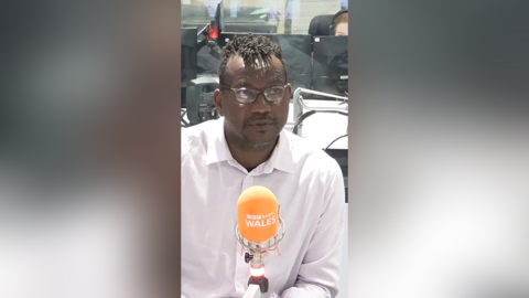 Joseff Gnagbo in a radio studio in a pink shirt with an orange microphone