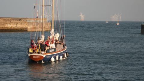 Sailing boat in the water with wind turbines in the background