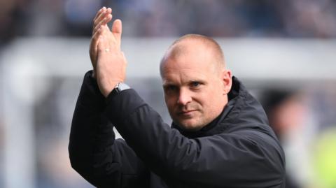 Huddersfield Town boss Liam Manning raises his hands to applaud supporters
