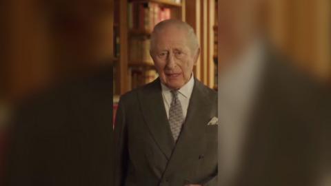 King Charles is wearing a grey suit with a white shirt and a lighter grey tie