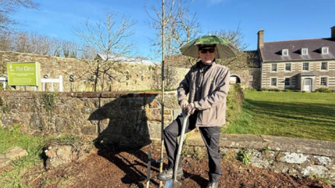 A picture of a man with a large spade and wearing wellies. A man is pictured in front of a house.