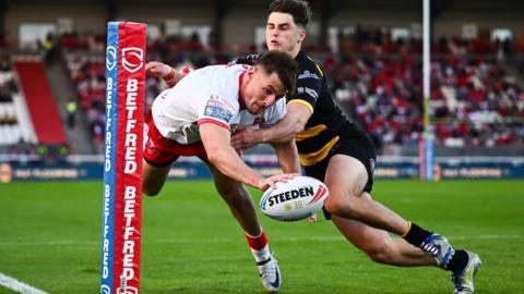 Hull KR winger Tom Davies reaches out with the ball in one hand as he dives towards the line under a challenge from a York Knight player