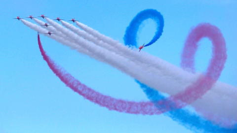 Eight Red Arrows jets in flight with red, white and blue smoke trailing from them