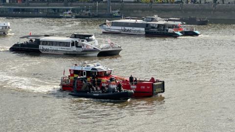 A fire boat is towing a black rigid police vessel on the River Thames in central London.