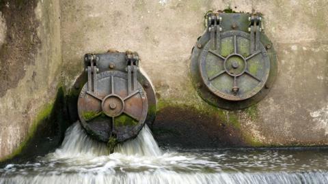 Water discharges from two cylindrical utlet pipes into the River Mersey next to the United Utilities waste water treatment plant in Stretford on June 23, 2025 in Manchester