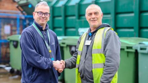 Medway Maritime hospital worker James Heather (left) with grey hair and glasses shaking hands with his colleague Eddie Butler (right) who is wearing a hi vis jacket