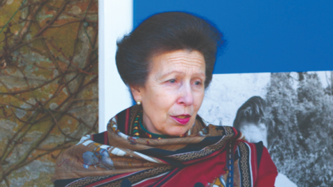 A picture of the Princess Royal speaking at Durrell at a previous year. She is wearing a red outfit with a sign behind her.