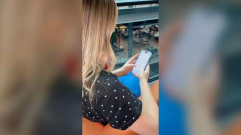 The back of a blonde woman's head scrolling on a smart phone