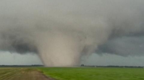 A large tornado is seen moving across a green field in a vertical photo