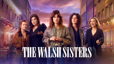 5 female family members stand in the middle of a lit up street at night time
