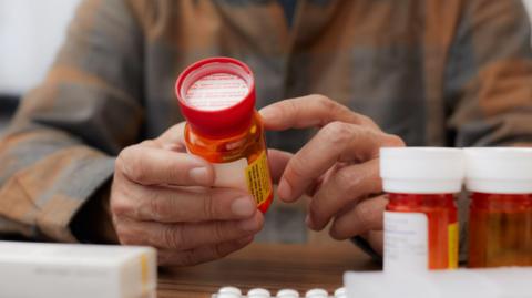 Close-up of a senior man's hands holding a prescription bottle and reading the label