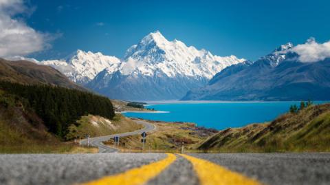 A winding road with water and mountains in the background in New Zealand.