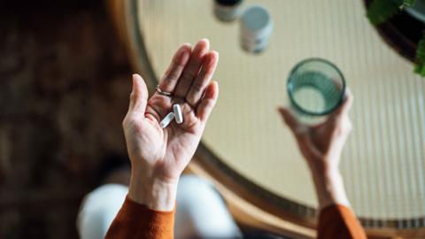 An aerial image of a woman holds two tablets in her left hand and a glass of water in her right.