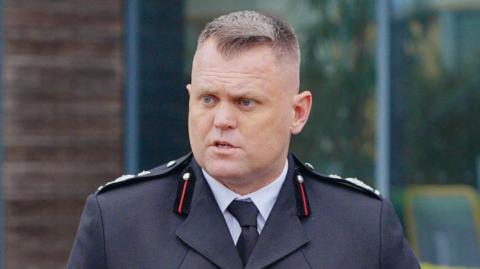 Nathaniel Hooton, deputy chief fire officer at Gloucestershire Fire and Rescue, in his uniform, looking to the side. He has short brown hair and is standing outside.