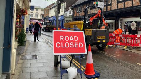 A sign in a town centre. It is a rainy, grey day. 