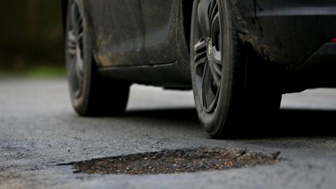 A black car driving past a pothole in the road.