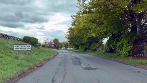 A general view of the A6105 near East Gordon. There is a road sign on the left and trees lining the road on the right.