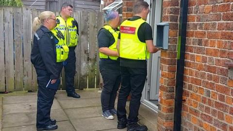 Noise enforcement officers and police stand outside the door of a property