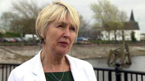 Siân Gwenllian stood in Cardiff Bay looking to the right of the picture, wearing a white jacket.