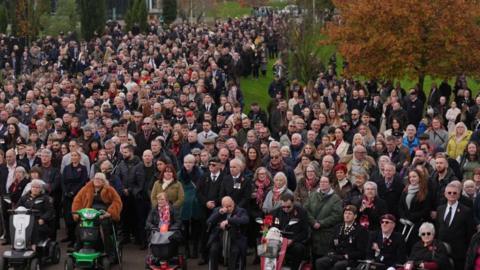 A large group of people stand or sit in silence during the Remembrance Sunday service at the National Memorial Arboretum. 