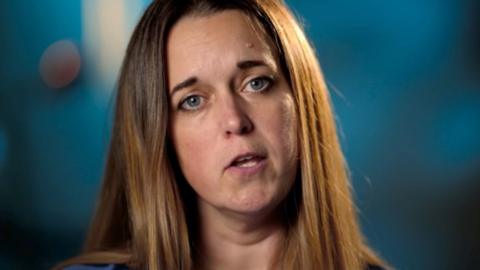 Woman with light brown hair looks towards camera