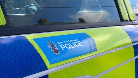 The door of a blue and yellow-liveried Devon and Cornwall Police car.