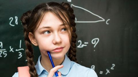 A 10-12-year-old schoolgirl is thinking while standing in front of a blackboard.