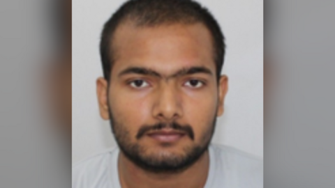 Custody photo of Pankaj Lamba against a grey background. He has dark facial hair, brown eyes and is looking at the camera.