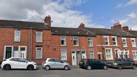 A row of terraced houses, with cars parked outside of them. 