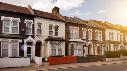 The photos show a street with a row of terraced houses. Each has a front door, a large ground floor window and two smaller first floor windows. They have small front gardens separated from the pavement by a wall or hedge. It's a sunny day and the sunlight shines on the houses from the top right hand corner.